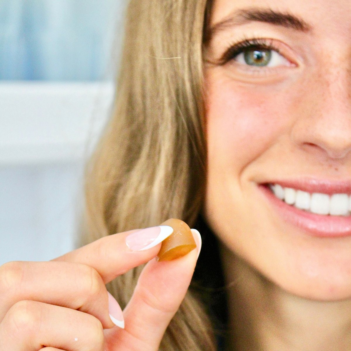 A woman holding a single gum drop shaped gummy next to her face